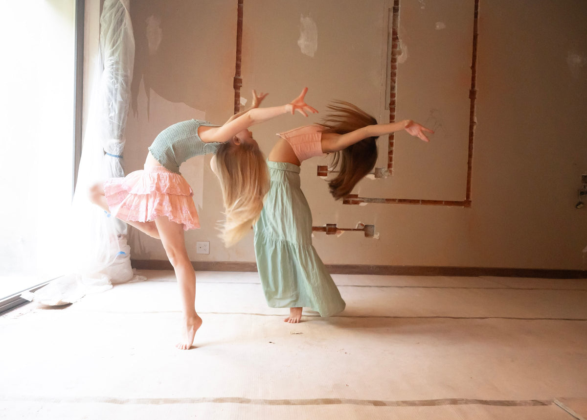 Dos figuras arqueadas hacia atrás, faldas rosa palo y verde agua en movimiento — campaña Bailarinas, Amor Amore