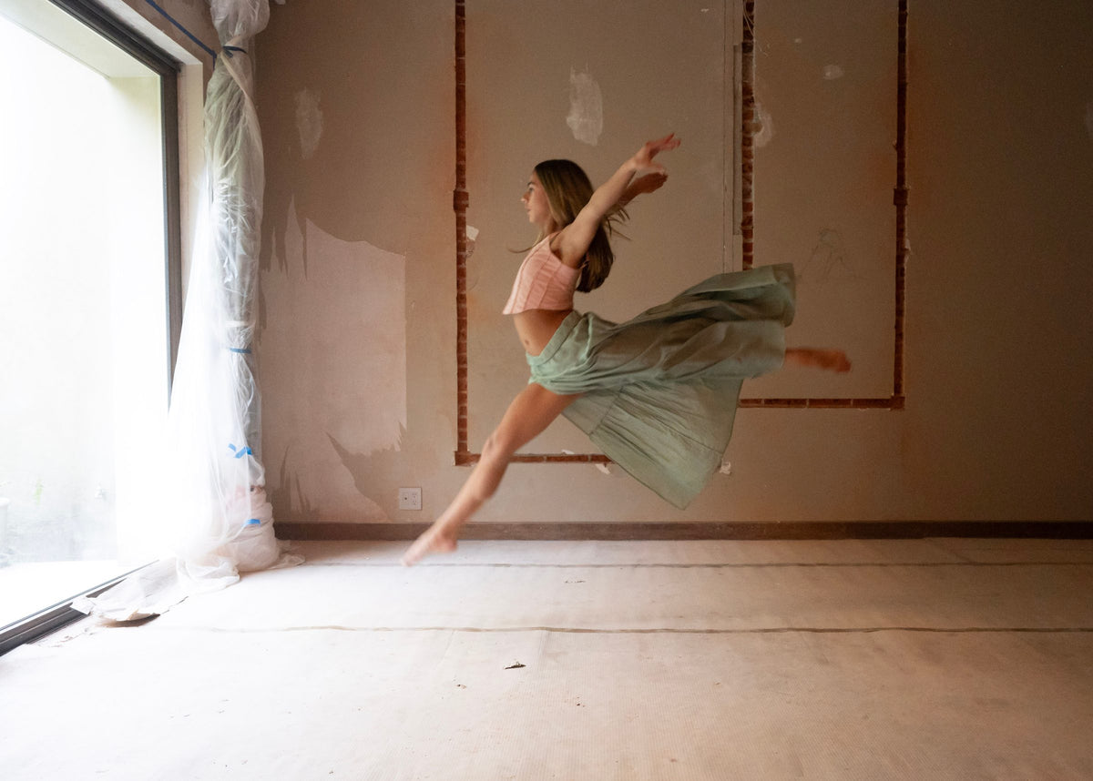 Salto con pierna extendida y falda verde agua flotando, brazos hacia arriba — campaña Bailarinas, Amor Amore