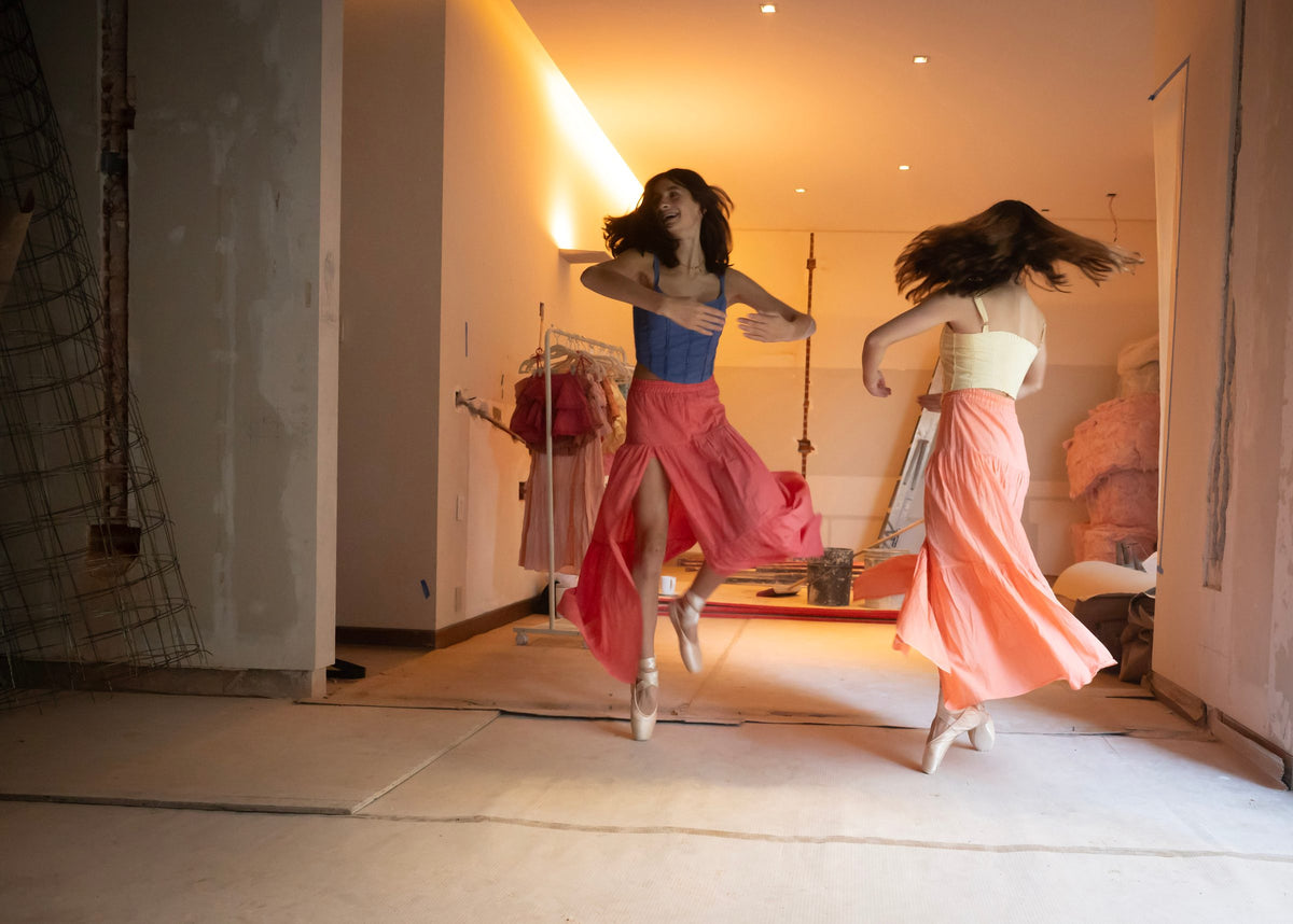 Dos giros simultáneos con faldas largas rosa al vuelo y tops de tirantes — campaña Bailarinas, Amor Amore