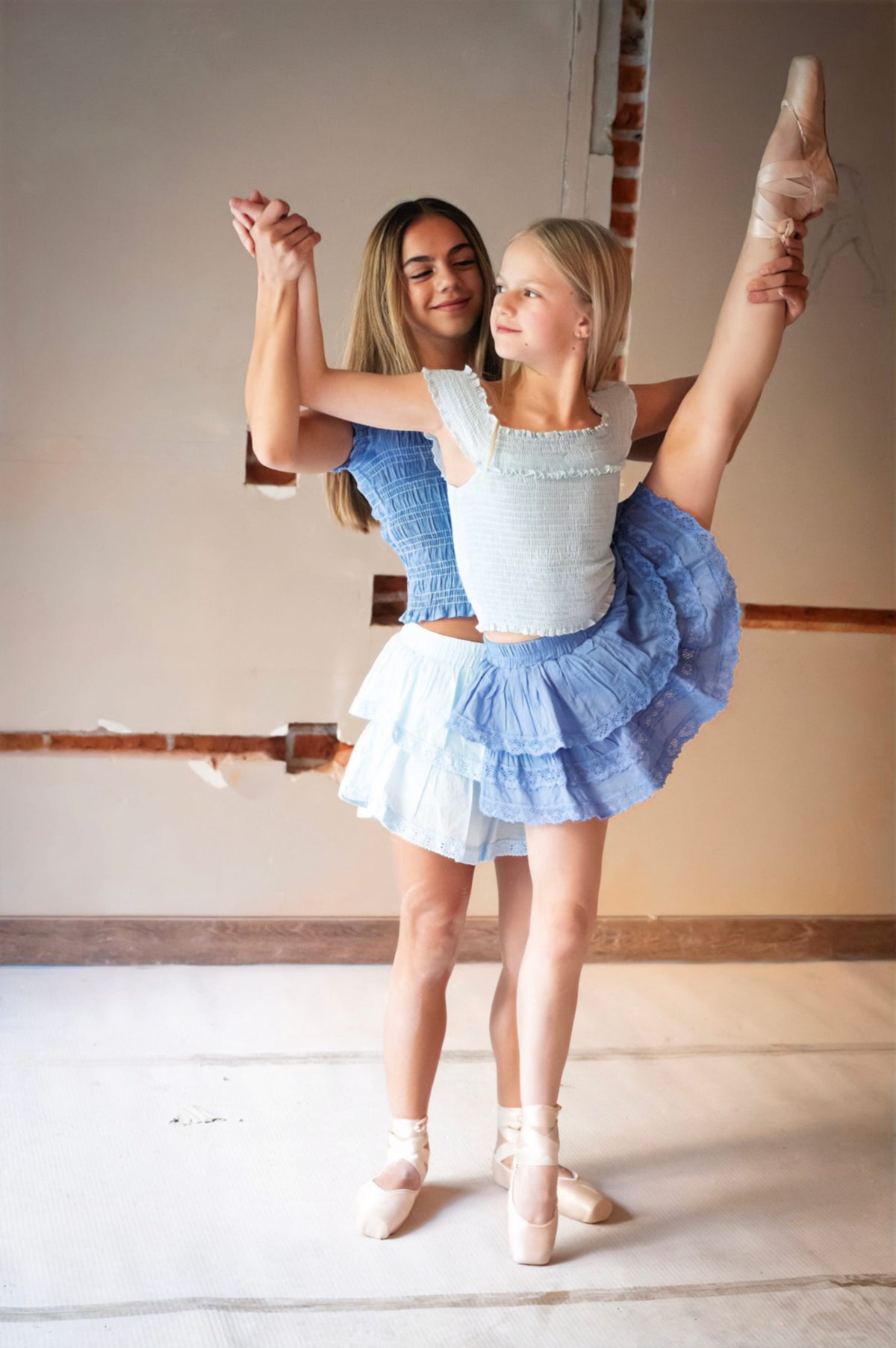 Dos figuras en pareja con una pierna elevada, faldas escalonadas azul y blanco — campaña Bailarinas, Amor Amore