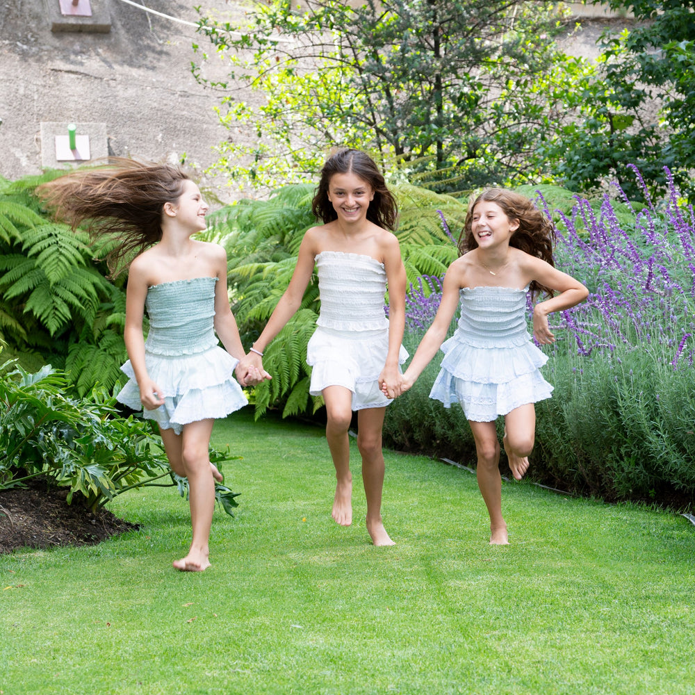 Tres conjuntos de top strapless verde agua corriendo de la mano por el jardín — campaña Bosque, Amor Amore