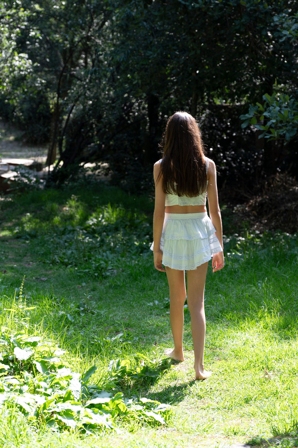 Top y falda blancos de espaldas en un claro de pasto rodeado de árboles — campaña Bosque, Amor Amore