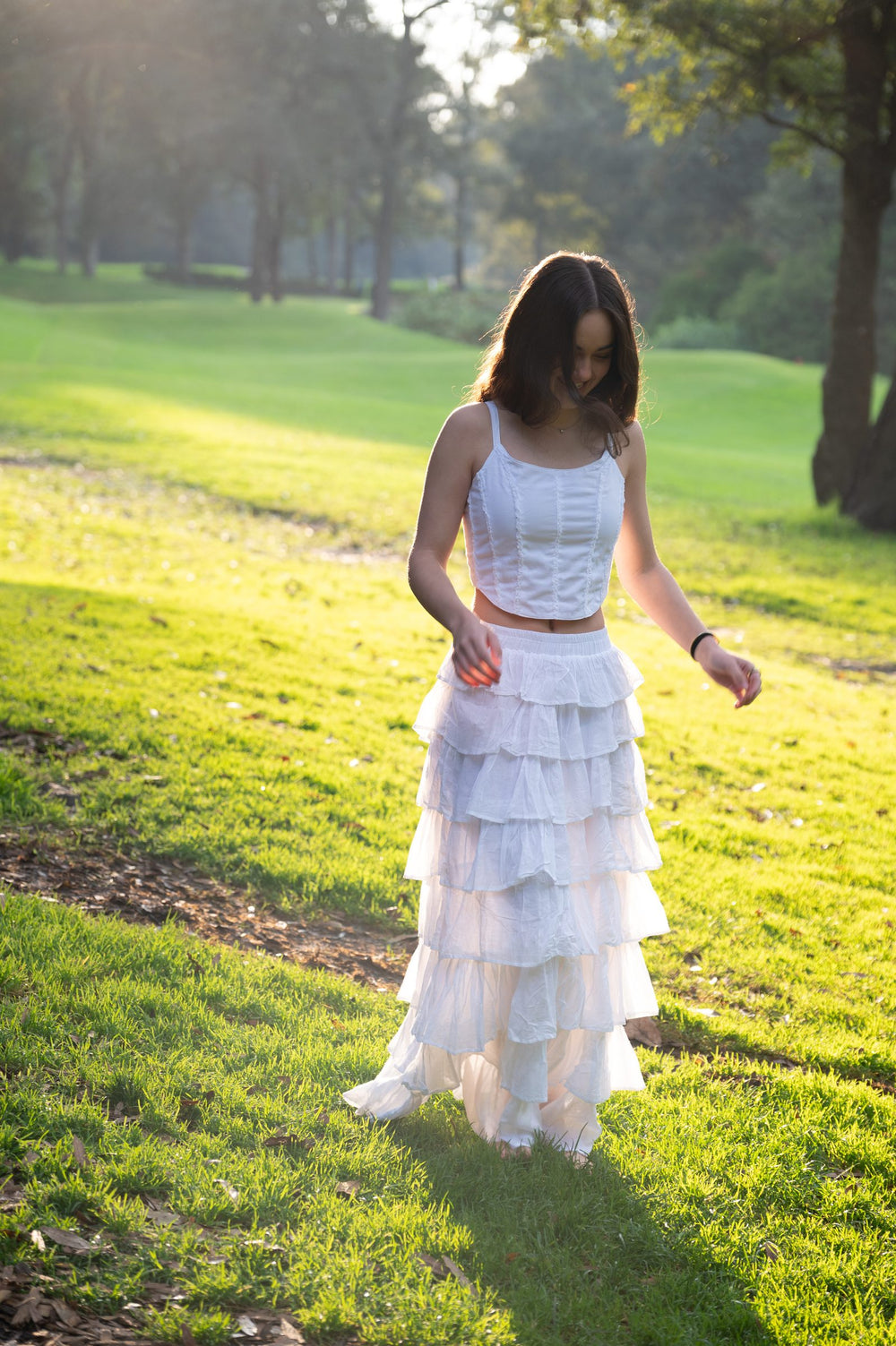 Conjunto blanco de top de tirantes y falda larga escalonada caminando por el parque — campaña Bosque, Amor Amore
