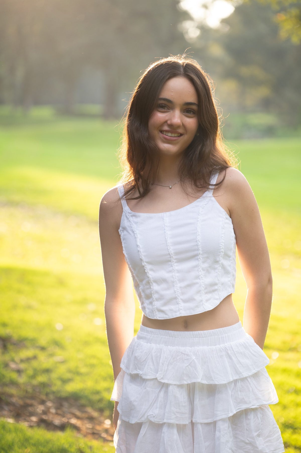 Top blanco de tirantes con falda corta de olanes en el parque a contraluz — campaña Bosque, Amor Amore