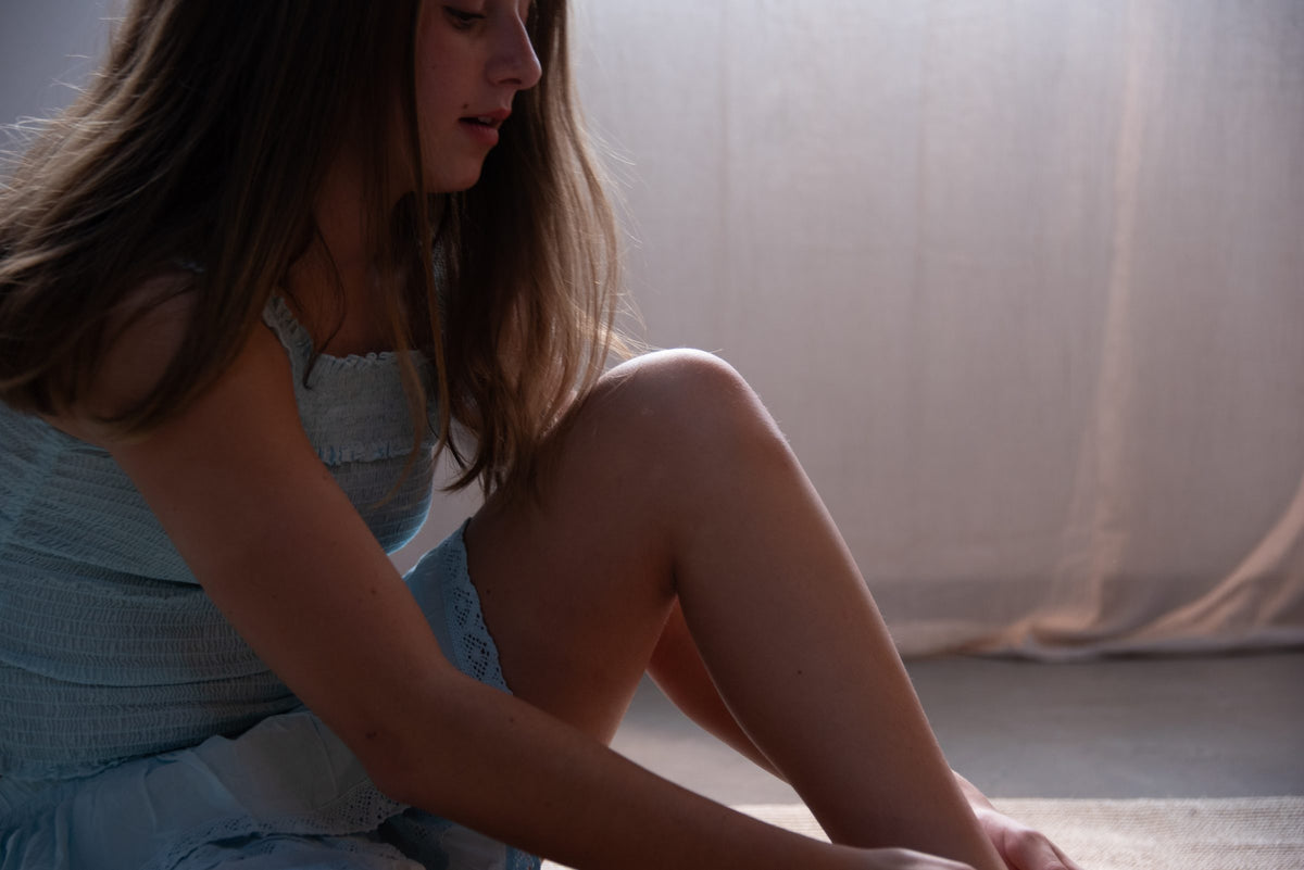 Sentada en el piso junto a la cortina del probador, con conjunto azul fruncido — campaña Collabs, Amor Amore