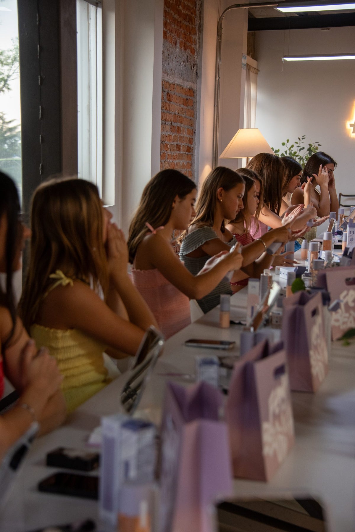 Conjuntos sentados a lo largo de la mesa larga del showroom junto al muro de ladrillo — campaña Collabs, Amor Amore