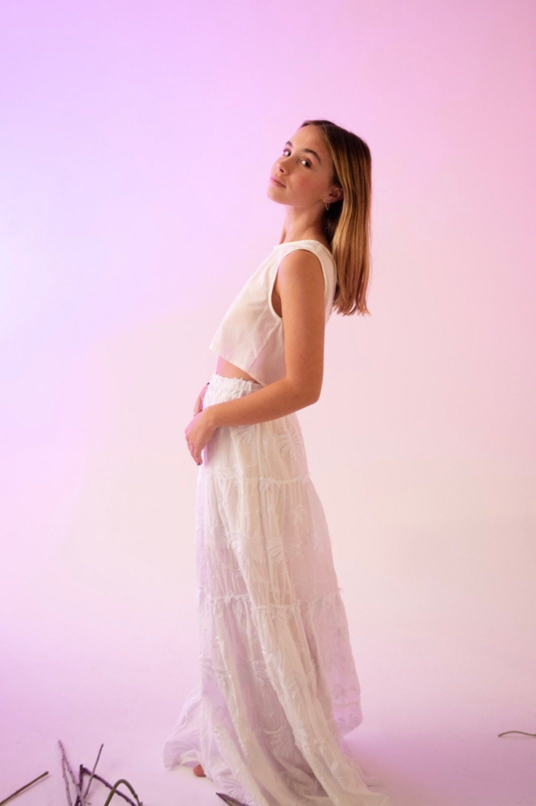 Perfil de falda larga blanca de encaje calado con top de tirantes, fondo rosa palo — campaña Estudio, Amor Amore