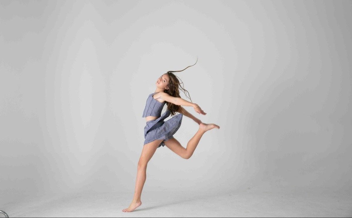 Salto de danza con pierna flexionada y conjunto gris azulado, fondo gris — campaña Estudio, Amor Amore