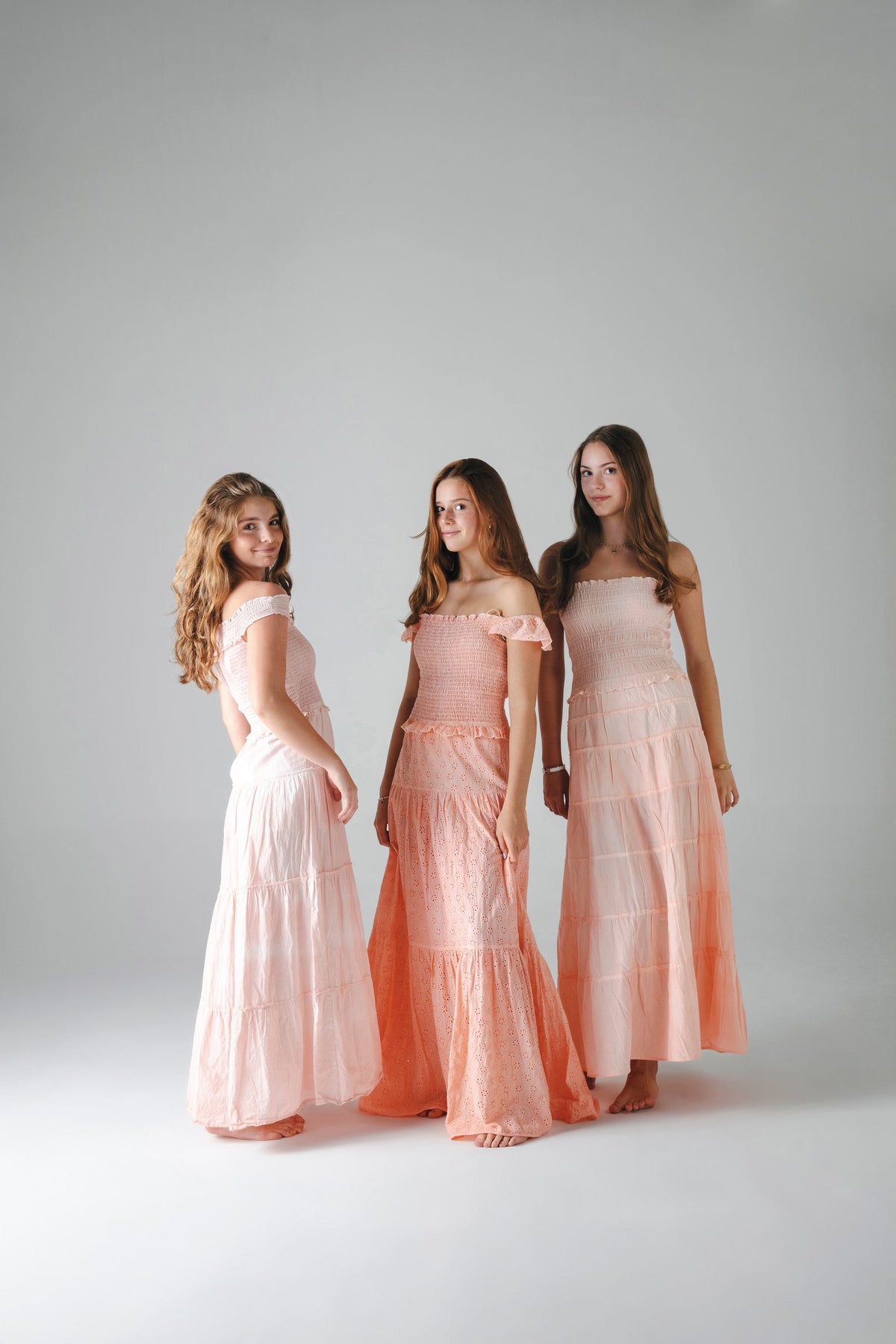 Tres faldas largas escalonadas en rosa palo y naranja, de pie sobre fondo gris — campaña Estudio, Amor Amore