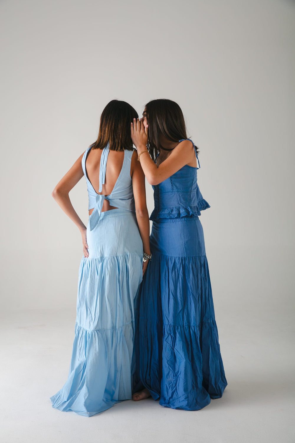 Dos faldas largas azules de espaldas, una azul claro y otra azul intenso, fondo gris — campaña Estudio, Amor Amore