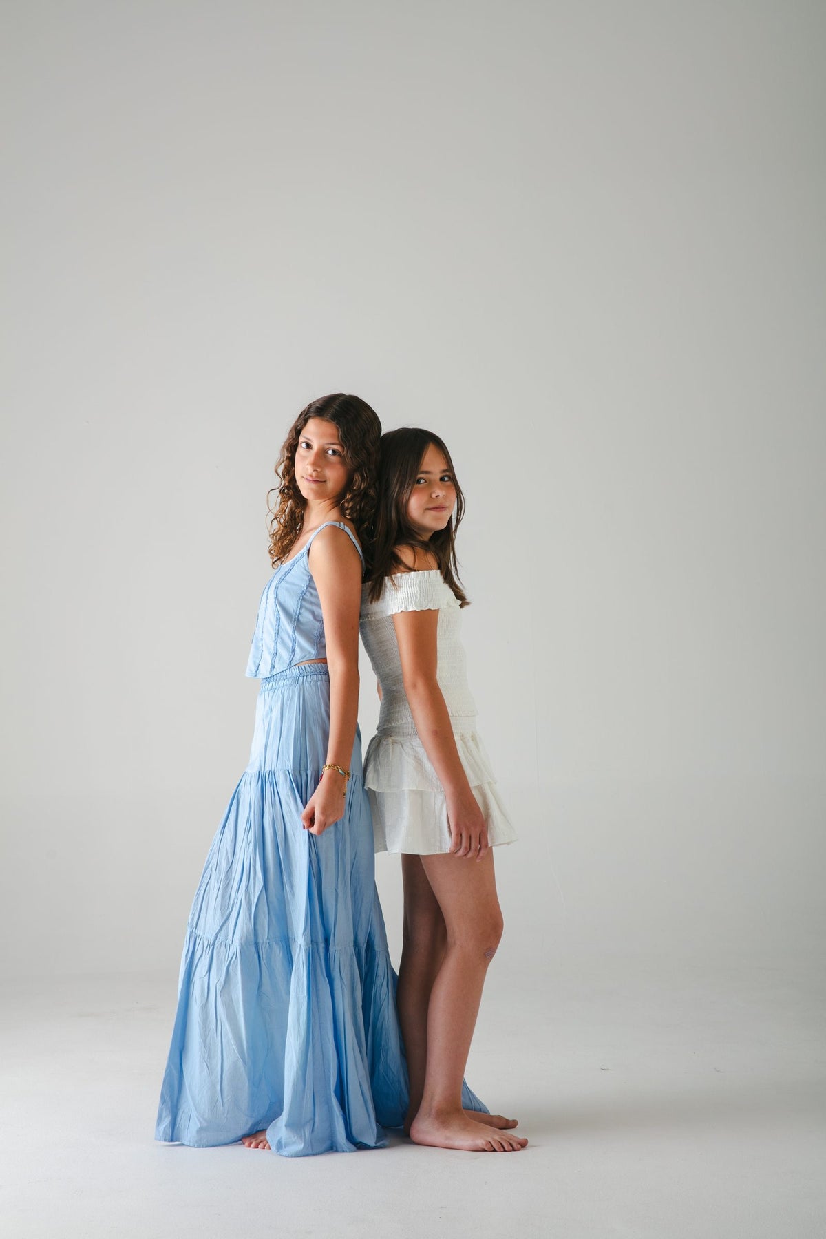 Falda larga azul y conjunto blanco corto, espalda con espalda sobre fondo gris — campaña Estudio, Amor Amore