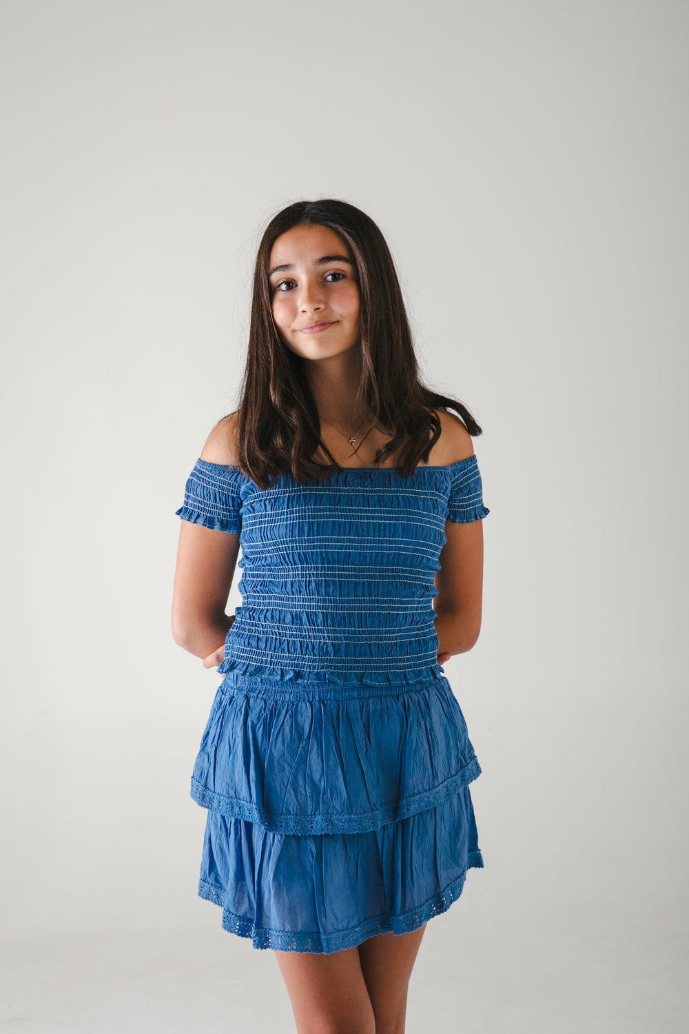 Conjunto azul de top de hombros descubiertos con manga y falda corta de olanes, fondo gris — campaña Estudio, Amor Amore