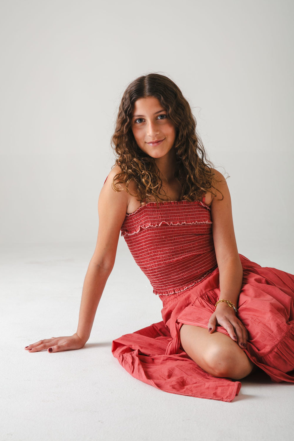 Sentada en el piso con top strapless fruncido vino y falda larga extendida, fondo gris — campaña Estudio, Amor Amore