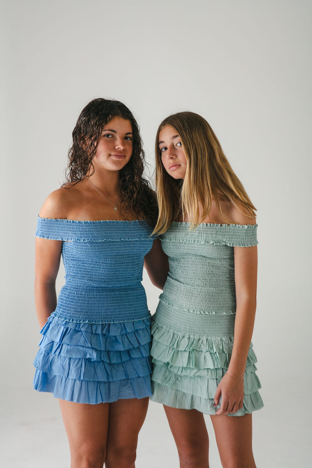 Dos conjuntos de hombros descubiertos con falda corta de olanes, azul y verde agua, recargados — campaña Estudio, Amor Amore