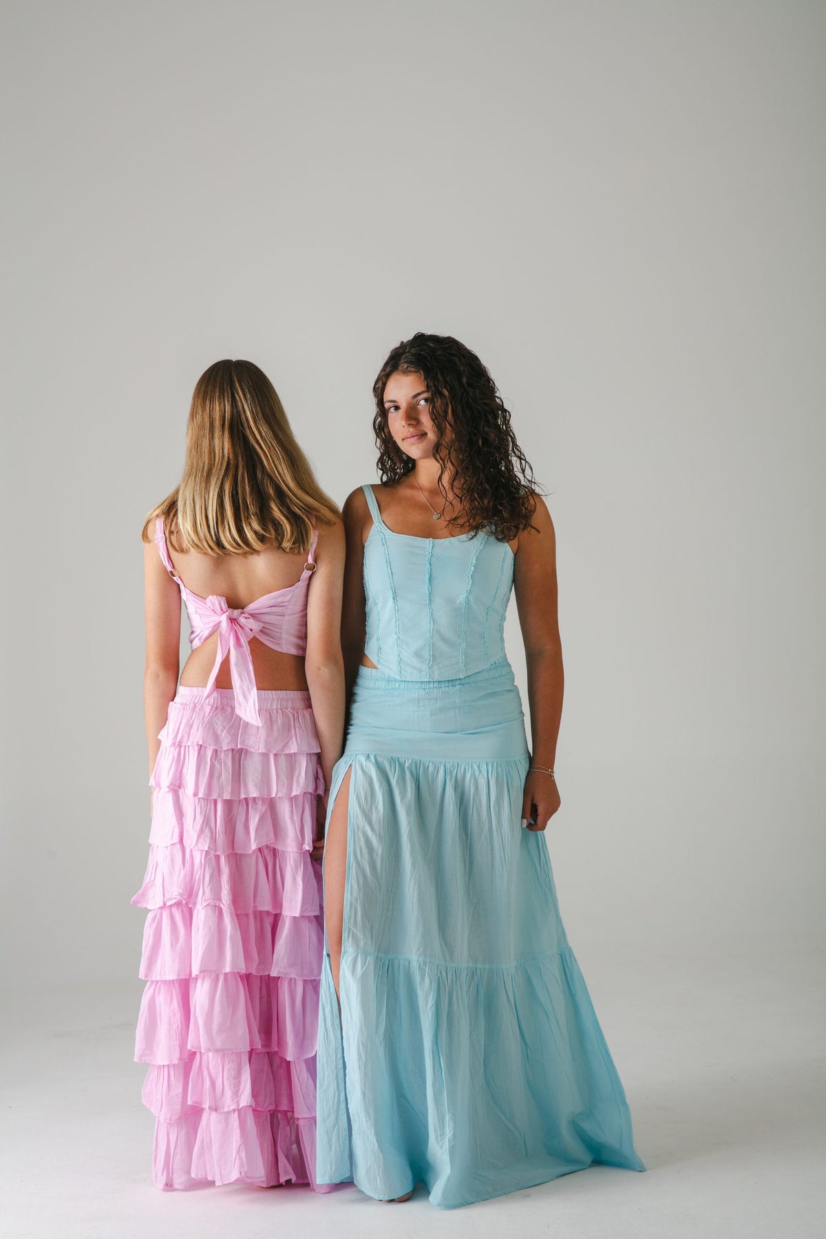 Falda larga rosa de olanes vista de espaldas junto a conjunto turquesa con falda con abertura — campaña Estudio, Amor Amore