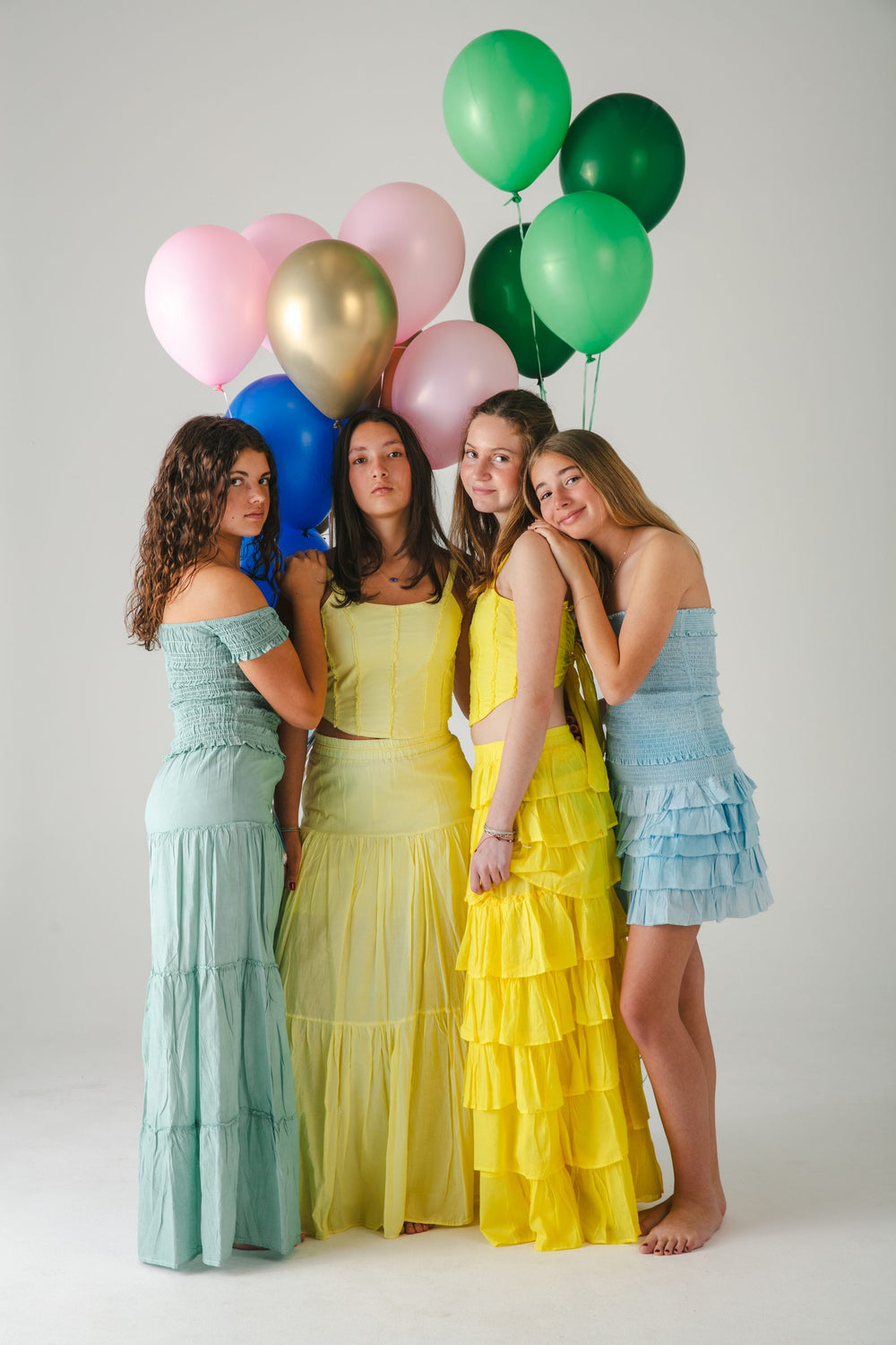 Cuatro conjuntos en verde agua, amarillo y azul, de pie con globos de colores atrás — campaña Estudio, Amor Amore