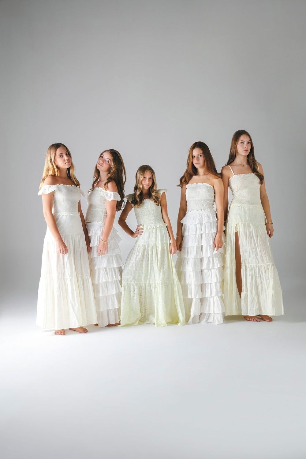 Cinco faldas largas blancas y beige de pie juntas, con tops fruncidos, fondo gris — campaña Estudio, Amor Amore
