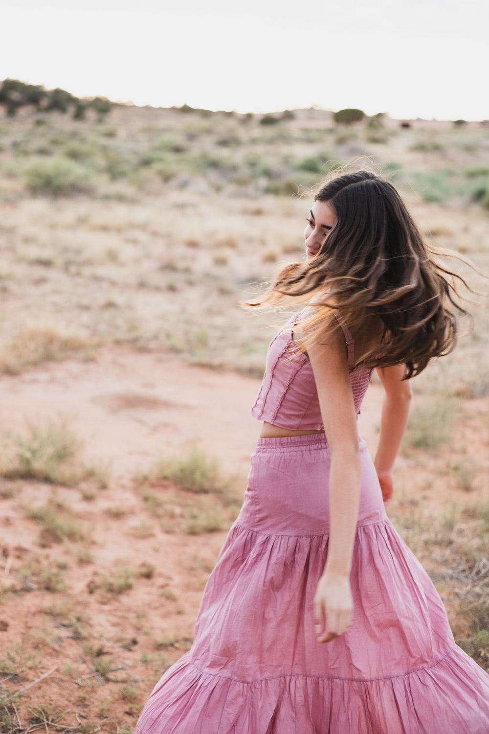 Falda larga escalonada rosa palo girando en el llano, con la mirada hacia atrás — campaña Montaña, Amor Amore