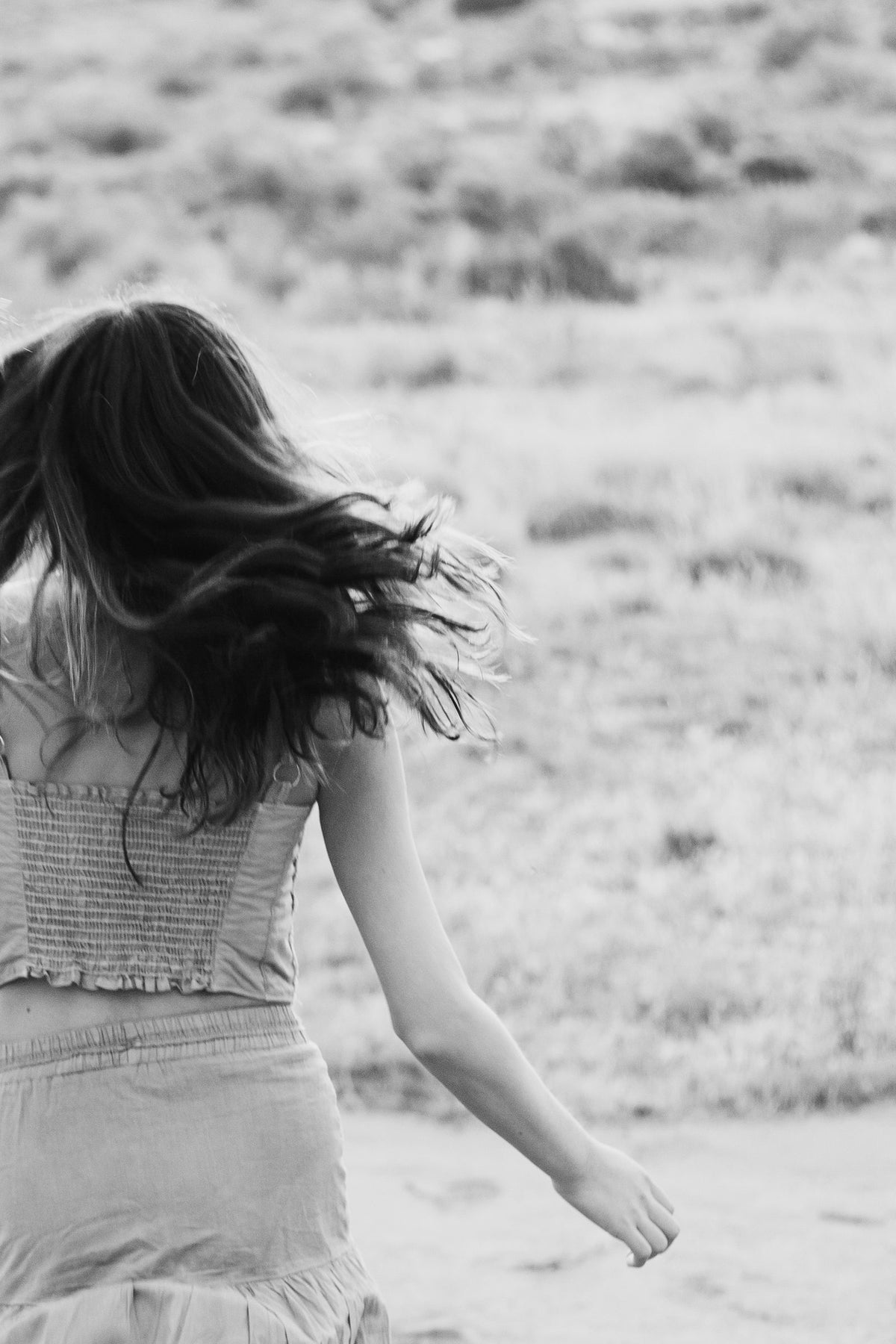 Blanco y negro de espaldas, top de cuerpo fruncido y cabello volando en el llano — campaña Montaña, Amor Amore