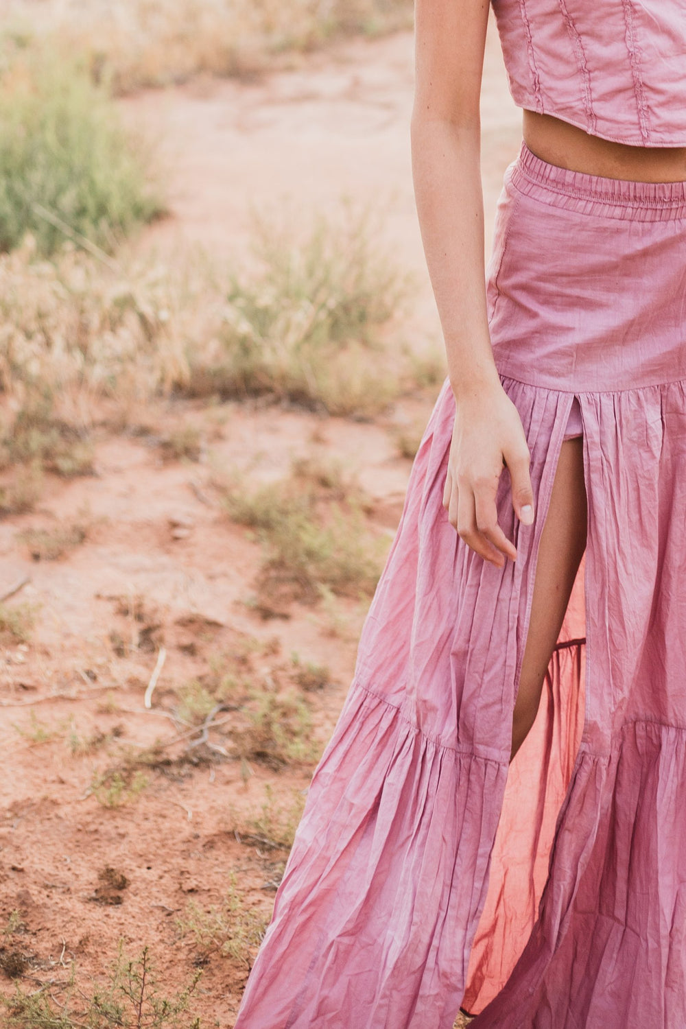 Detalle de la abertura de la falda larga escalonada rosa palo sostenida con la mano — campaña Montaña, Amor Amore