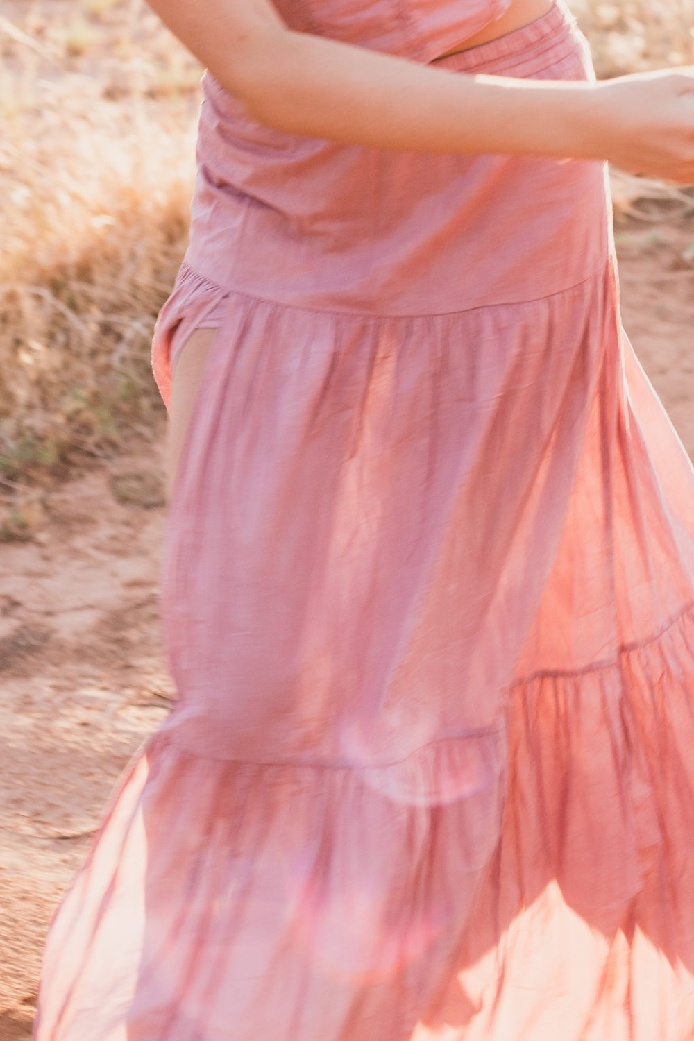 Detalle de la falda larga escalonada rosa palo en movimiento sobre el camino — campaña Montaña, Amor Amore
