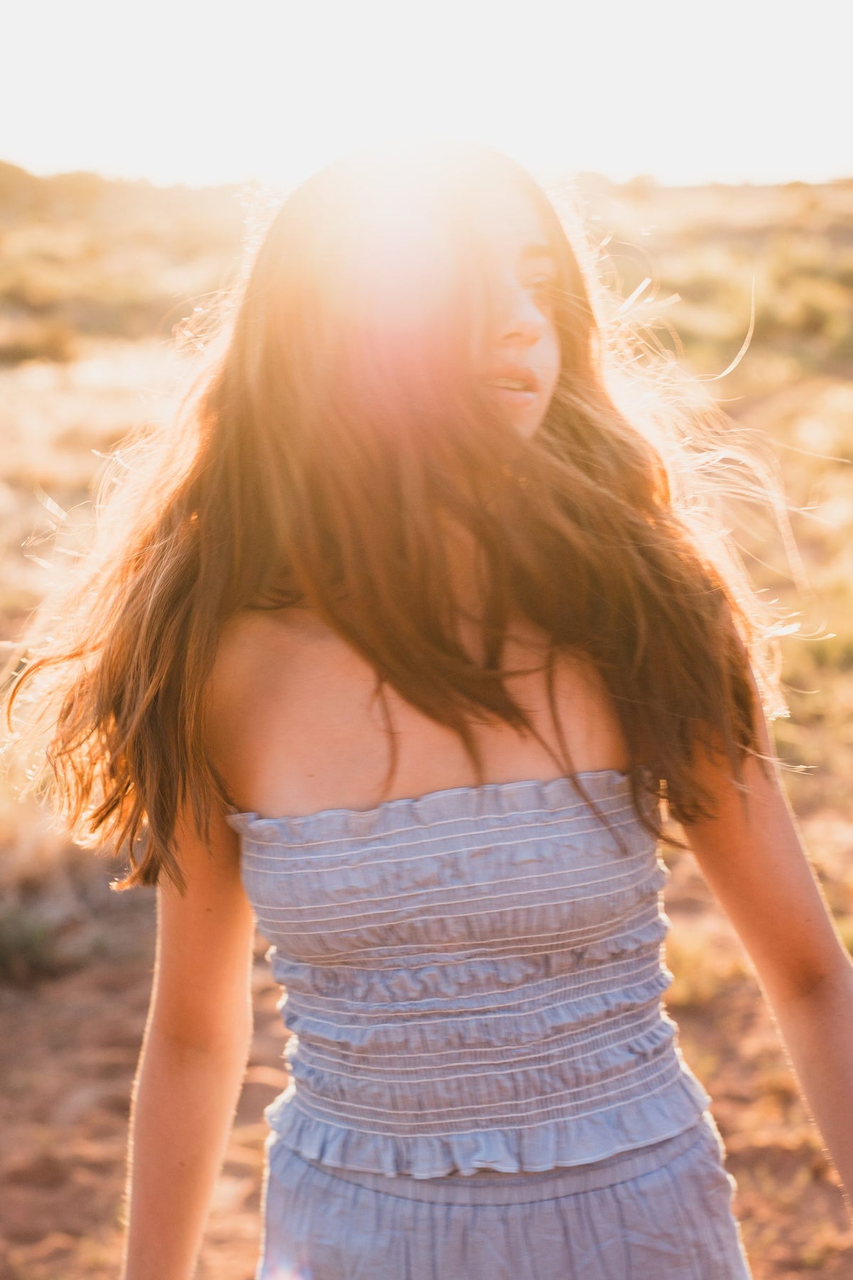 Top strapless azul fruncido con el cabello cubriendo el rostro y el sol al fondo — campaña Montaña, Amor Amore