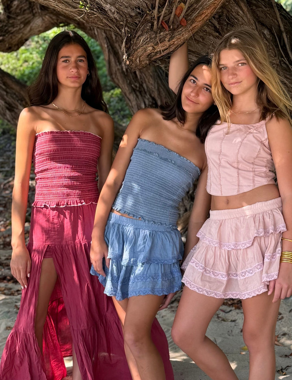 Tres conjuntos bajo un árbol de la playa: una falda larga con abertura y dos cortas de olanes — campaña Playa, Amor Amore