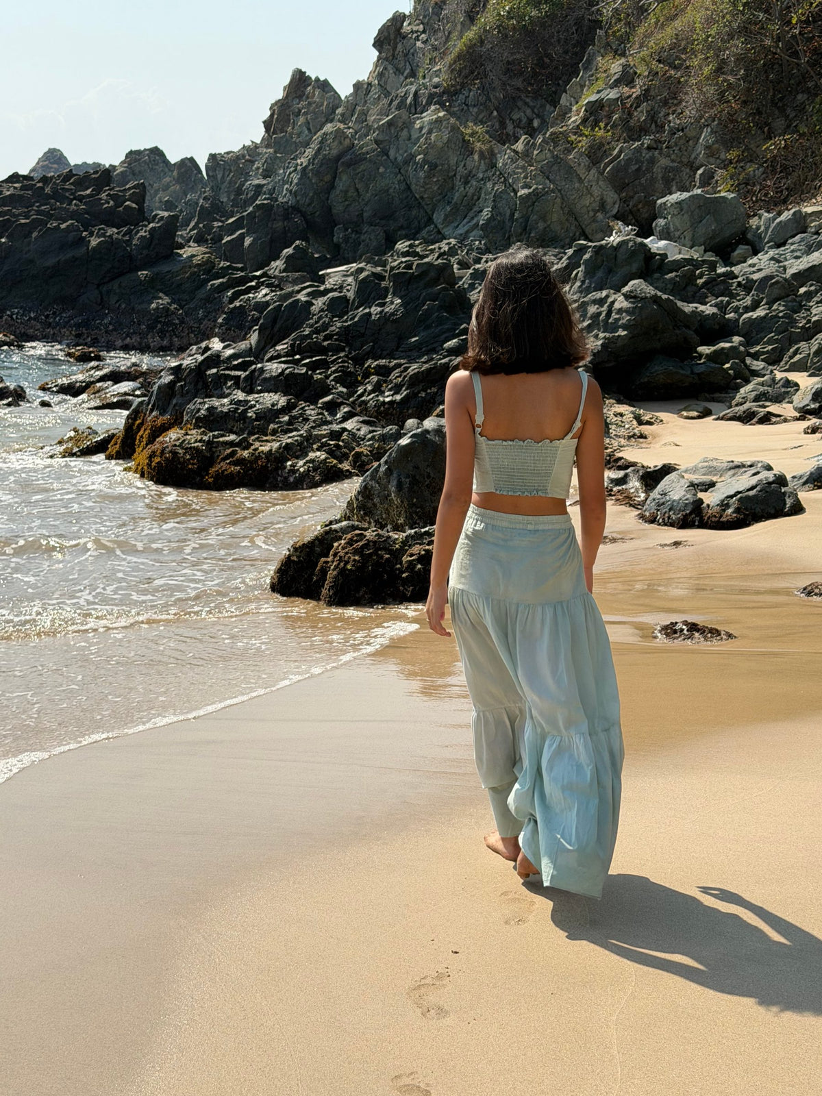 Conjunto largo verde agua de espaldas, caminando hacia las rocas — campaña Playa, Amor Amore