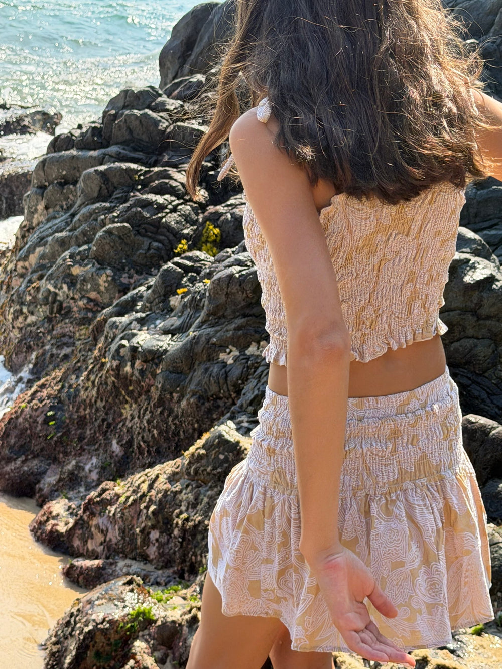 Conjunto corto estampado de espaldas, entre las rocas y el agua — campaña Playa, Amor Amore